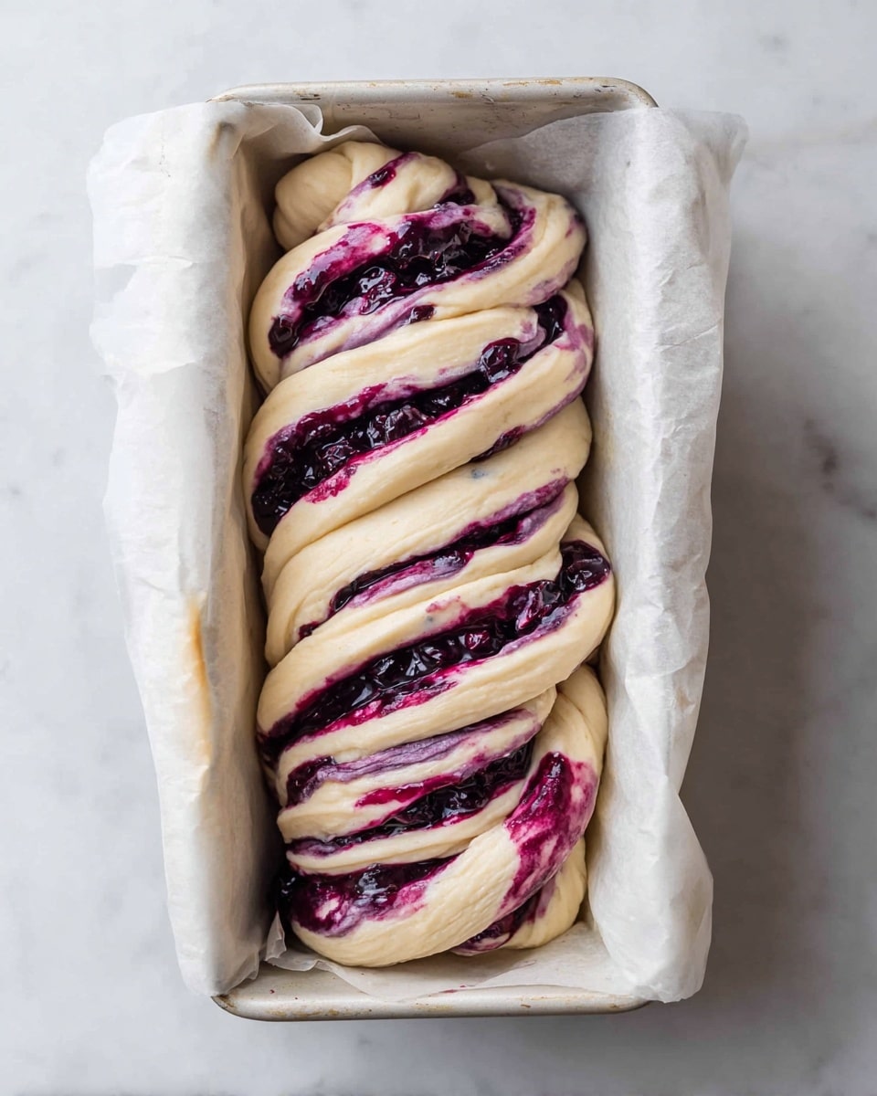 A twisted loaf of dough filled with dark purple mixed berry filling is placed inside a white parchment-lined loaf pan. The dough is light cream color with a soft and smooth texture, twisted multiple times to reveal thick swirls of deep purple and dark blue berries running through every twist. The loaf pan sits on a white marbled surface, with the parchment paper gently folded around the edges of the dough, creating a cozy nest. The berries appear juicy and slightly chunky, contrasting against the pale dough layers. photo taken with an iphone --ar 4:5 --v 7