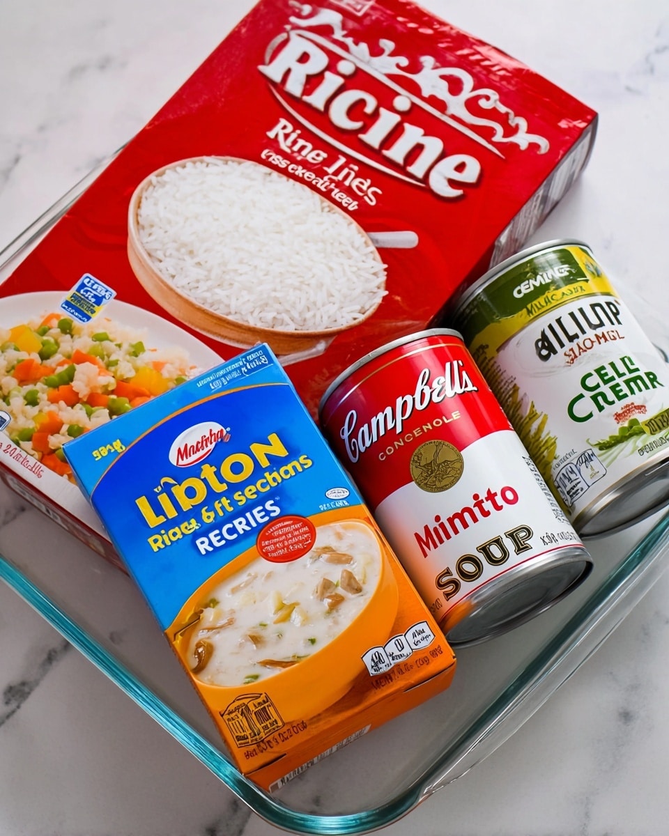 The image shows four cooking ingredients placed inside a clear rectangular glass dish set on a white marbled surface. In the back left, there is a large red box of Minute white rice with white rice grains and vegetables visible on the front. In front of the rice box, a smaller blue and orange box of Lipton Recipe Secrets Onion Soup & Dip Mix is angled slightly, showing an image of creamy onion dip with celery sticks. To the right, two cans of Campbell's soup are lying down, with one labeled