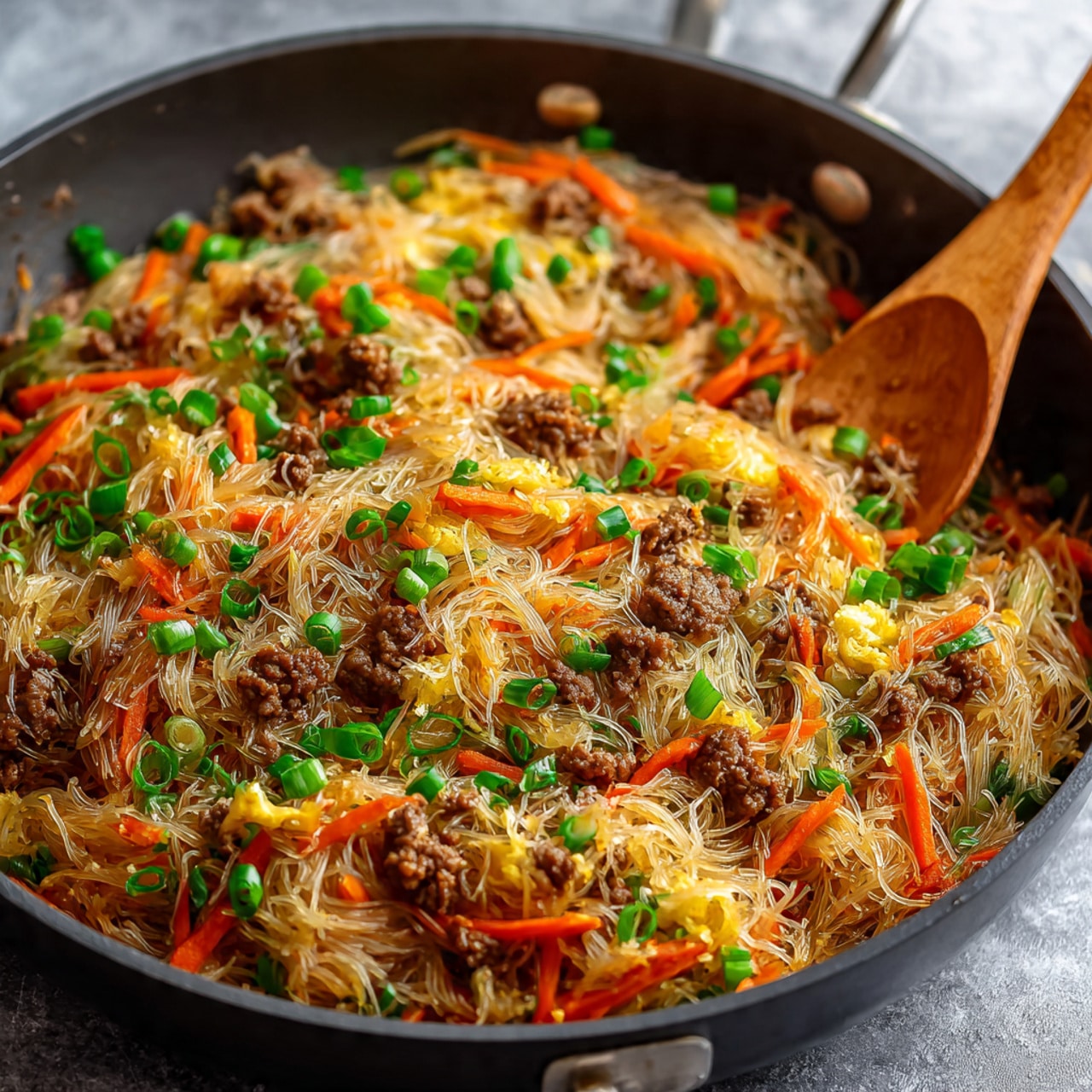 The image shows a white square plate filled with a large serving of thin rice noodles mixed with several shrimp scattered throughout. The noodles are light beige and slightly glossy, topped with bright red sauce dollops placed unevenly across the dish. There are pieces of green onions sprinkled all over, adding small green pops of color, along with thin orange carrot strips mixed into the noodles. Small sesame seeds are scattered on top, providing texture and contrast. The plate sits on a white marbled surface. Photo taken with an iphone --ar 4:5 --v 7