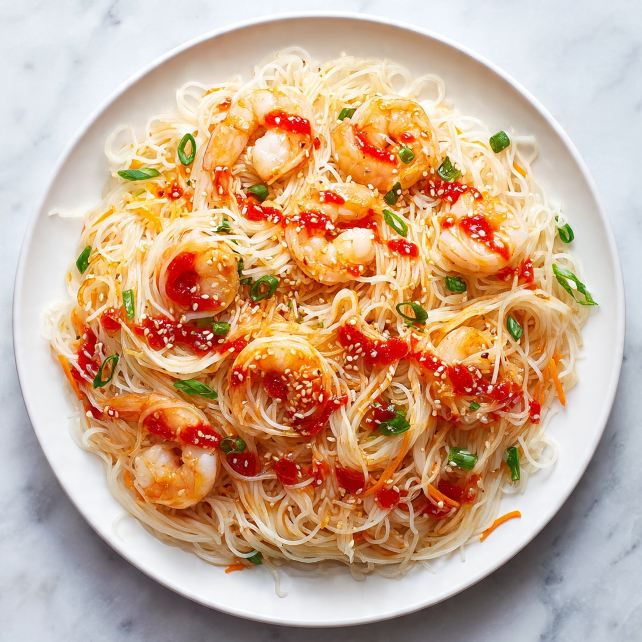 The image shows a white plate on a white marbled surface holding three golden brown spring rolls placed in a neat row on the right side. On the left side of the plate is a round pile of thin, light brown noodles mixed with shredded carrots and cabbage, giving the dish a mix of warm beige, orange, and pale yellow colors. Above the noodles, there is a small clear glass bowl filled with a bright red dipping sauce. To the right of the plate lies a pair of wooden chopsticks parallel to each other. Photo taken with an iphone --ar 4:5 --v 7