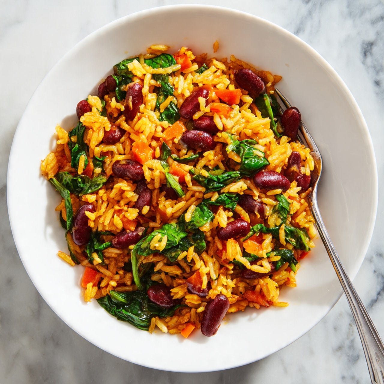 This image shows a close-up of a colorful rice dish with three main layers mixed together: bright yellow-orange rice, small dark red beans, and fresh green spinach leaves. There are also small orange pieces of carrot sprinkled throughout, adding a vibrant contrast. The textures of the rice appear soft and sticky, while the beans look smooth and firm, and the spinach leaves are tender and slightly shiny. A metal fork holds a small scoop of the mix in the scene, all set against a white marbled surface. photo taken with an iphone --ar 4:5 --v 7
