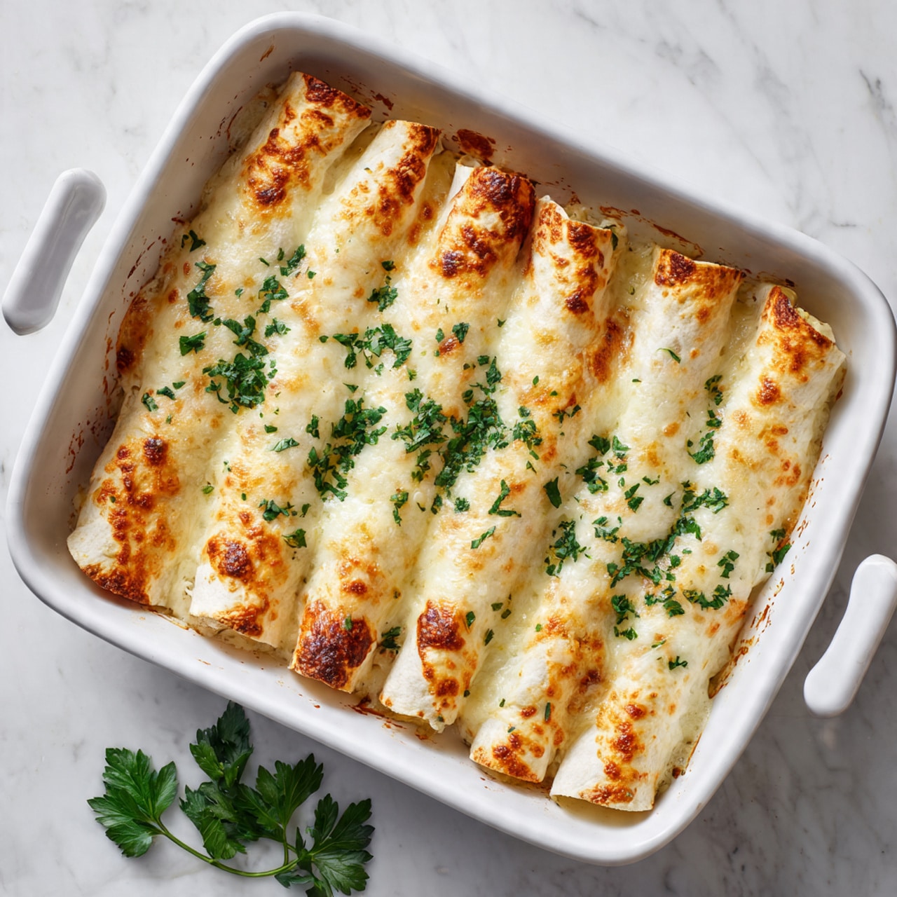 A white rectangular baking dish contains eight rolled tortillas lined up side by side, each covered with a melted, light golden cheese layer that has slightly browned edges. The cheese topping is smooth with a few small patches of darker yellow and light brown where it cooked more. Fresh green parsley leaves are sprinkled evenly over the cheese, adding color contrast. The dish is placed on a white marbled surface, with some parsley leaves casually scattered nearby. photo taken with an iphone --ar 4:5 --v 7