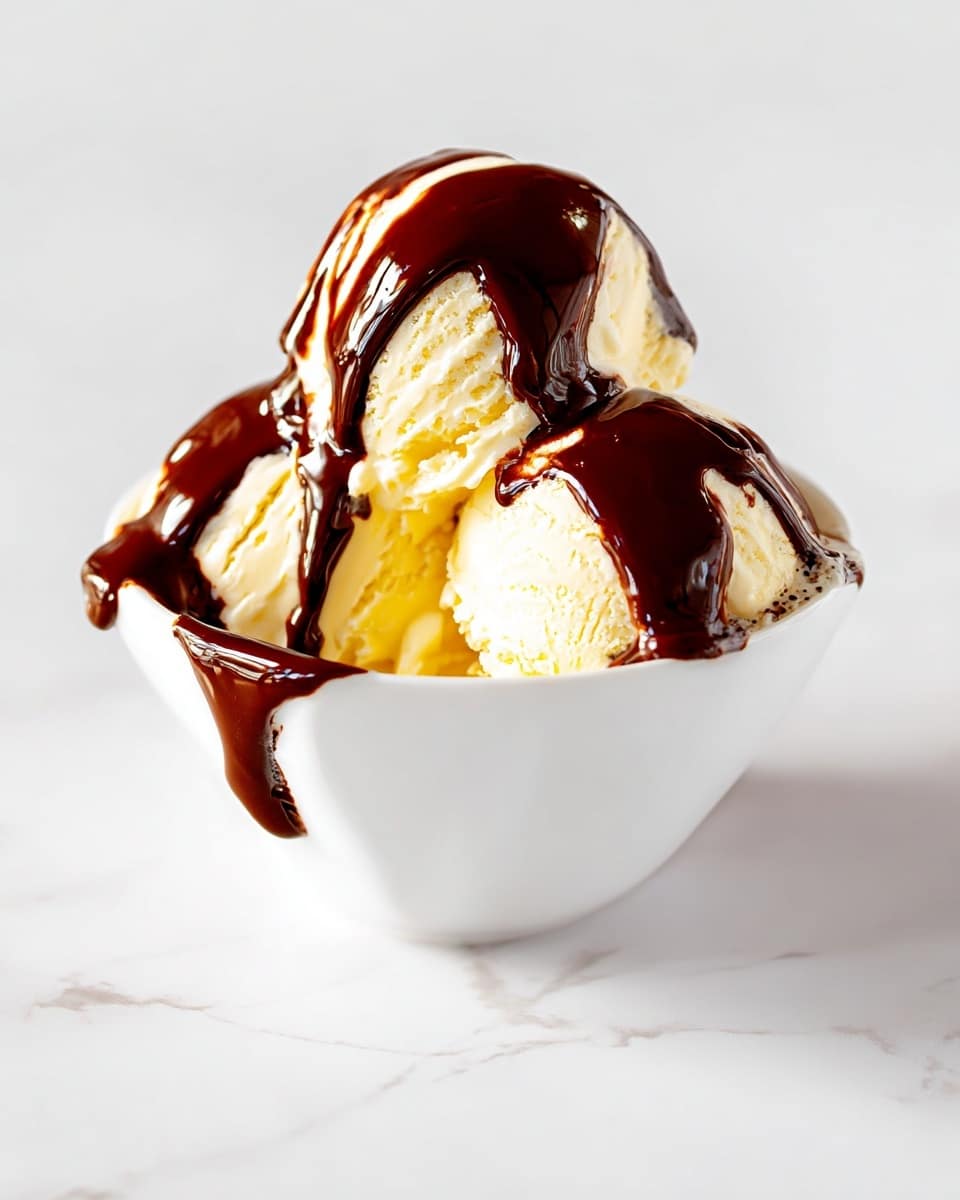 A white bowl holds three scoops of pale yellow vanilla ice cream, each scoop showing soft, creamy texture. Dark, shiny chocolate sauce generously covers the top of the ice cream, dripping down over the sides of the bowl and pooling on the white marbled surface below. The smooth chocolate's deep brown contrasts strongly with the light ice cream and the clean white bowl. The background is a simple, bright white marbled texture that keeps the focus on the dessert. photo taken with an iphone --ar 4:5 --v 7