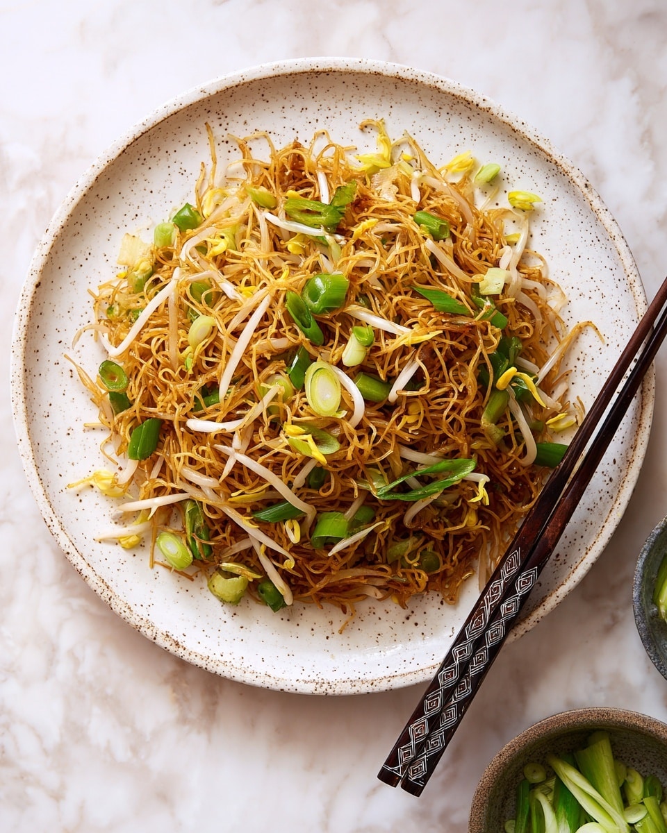 The image shows a round mound of stir-fried thin noodles on a white speckled plate. The noodles have a golden-brown color with some darker brown charred parts, creating a textured look. Mixed within the noodles are bright green pieces of scallion, pale white bean sprouts, and small yellow bean sprout heads, scattered throughout evenly. On the right side of the plate rest a pair of dark wooden chopsticks with diamond patterns. The background features a white marbled surface with a small bowl containing sliced green scallions partially visible near the bottom right corner. Photo taken with an iphone --ar 4:5 --v 7