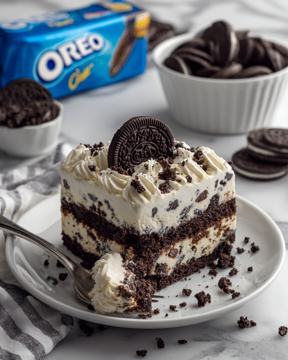 The image shows a rich Oreo dessert on a white plate with three visible layers: a dark, crumbly Oreo base at the bottom, a thick middle layer of creamy white filling mixed with Oreo chunks, and a top layer of smooth white whipped cream decorated with an Oreo cookie piece standing upright. Next to the dessert is a fork with a square bite of the dessert, showing the layers distinctly. In the background, a white bowl filled with whole Oreo cookies and a blue package of Oreos are visible, all sitting on a white marbled surface. There are some Oreo crumbs scattered around, adding texture to the scene. photo taken with an iphone --ar 4:5 --v 7