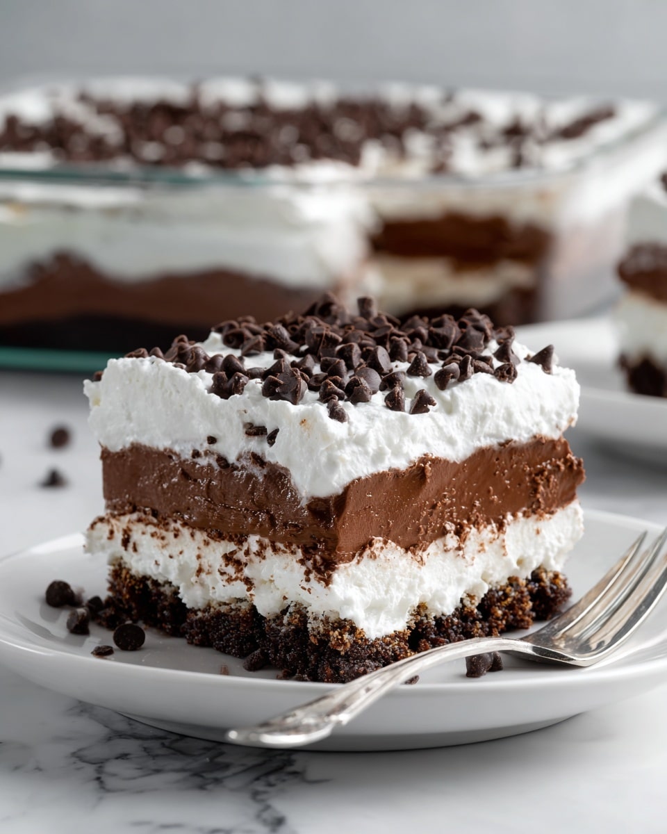 The image shows a layered dessert piece on a white plate with a silver fork beside it. The dessert has four clear layers: a bottom dark brown crumbly crust, a thick dark chocolate layer above it, a thick white whipped cream layer on top, and many small dark chocolate chips sprinkled all over the whipped cream. In the background, there is a glass baking dish with the same dessert, where one piece has been removed. The surface underneath everything is a white marbled texture. Photo taken with an iphone --ar 4:5 --v 7