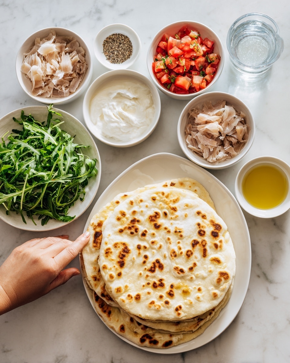 The image shows a white oval plate on the right side with a round flatbread that has light brown toasted spots and some specks of seasoning on top. Around the flatbread, there are small white bowls arranged neatly on a white marbled surface. The bowls contain different ingredients: one with arugula leaves that are fresh and green, another with diced red tomatoes mixed with small white pieces, one with thin slices of light brown meat, a bowl with smooth white sauce, and a small bowl with coarse black pepper. A small glass with golden olive oil and another small glass with clear water are also present. A woman's hand is reaching from the left towards the arugula bowl. photo taken with an iphone --ar 4:5 --v 7