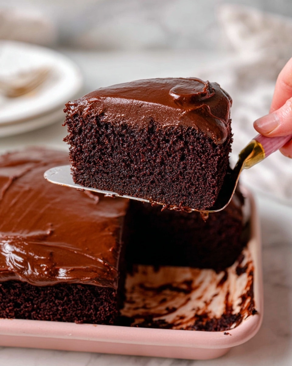 The image shows a slice of chocolate cake being lifted with a spatula by a woman's hand. The cake has two layers: a dark, moist chocolate base with a soft texture, and a thick layer of shiny, smooth chocolate frosting on top. The frosting is also spread on the cake in the baking tray beneath. The background is a white marbled texture with a white plate nearby, slightly out of focus. The spatula has a pink handle with a golden part near the blade. photo taken with an iphone --ar 4:5 --v 7