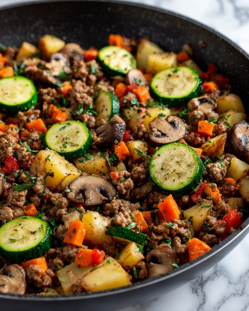 This dish shows a close-up of cooked ground meat mixed with various vegetables, all inside a dark pan. There are roughly chopped light green zucchini slices placed on the top right and bottom center, with visible seeds and bits of green herbs. Mixed in are small orange carrot pieces and dark brown mushrooms with smooth tops. Pale yellow potato chunks are scattered throughout, along with bits of red tomato. The whole mixture is lightly sprinkled with small green herb leaves, adding a fresh touch. The surface beneath the pan is a white marbled texture. Photo taken with an iphone --ar 4:5 --v 7