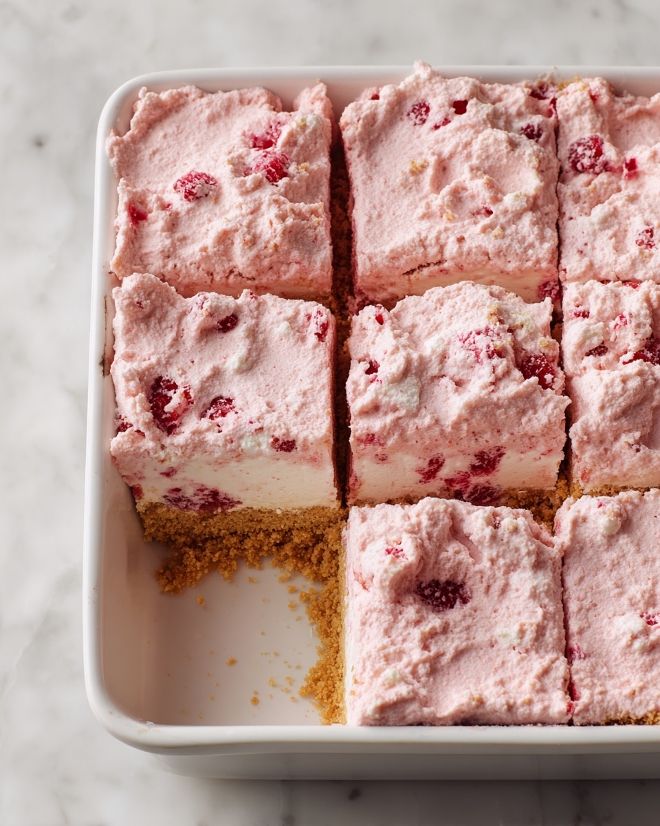 A white square dish holds pink dessert bars arranged in a grid with one bar missing near the center, exposing a thin golden brown crumbly crust underneath. The dessert has two visible layers: a dense, crumbly bottom layer in light golden brown, and a thick, textured creamy top layer in pale pink with visible white chunks and bits of red fruit mixed in. The pink cream layer is spread unevenly, showing softness and a slightly rough surface. The dish sits on a white marbled surface. photo taken with an iphone --ar 4:5 --v 7