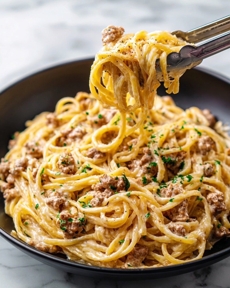 The image shows a close-up of creamy pasta with ground meat in a black bowl on a white marbled surface. The dish has one main layer: yellowish noodles mixed with small bits of brown ground meat, all coated in a light beige creamy sauce. Silver tongs hold a small serving of the pasta above the bowl, showing the noodles tangled and dripping with sauce and meat. The sauce looks smooth and thick, covering the noodles evenly. Photo taken with an iphone --ar 4:5 --v 7