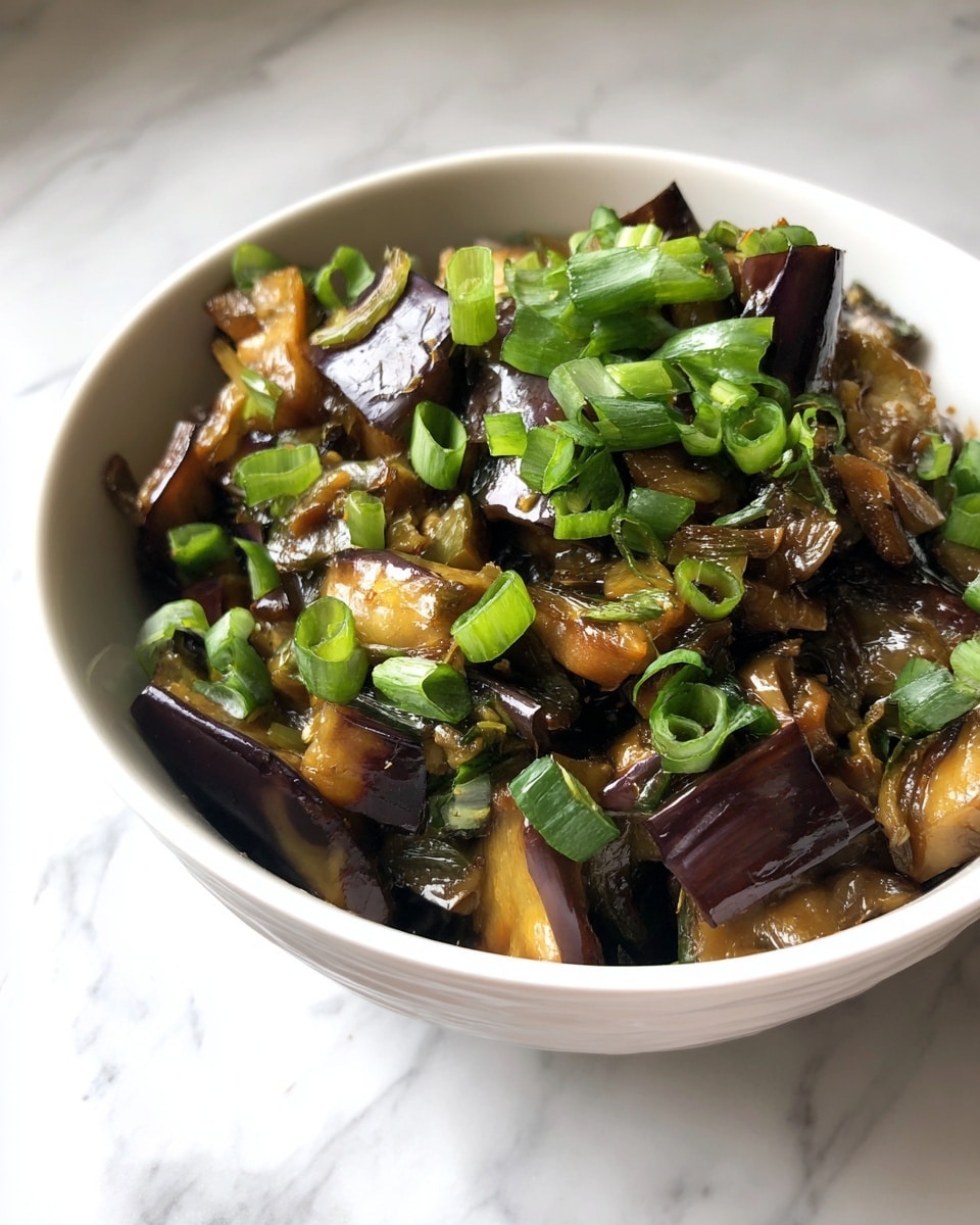 A white bowl filled with cooked eggplant pieces. The eggplants are dark brown with some shiny spots showing a cooked texture. Bright green chopped green onions are scattered on top, adding a fresh color contrast. The bowl is placed on a white marbled surface. The photo taken with an iphone --ar 4:5 --v 7