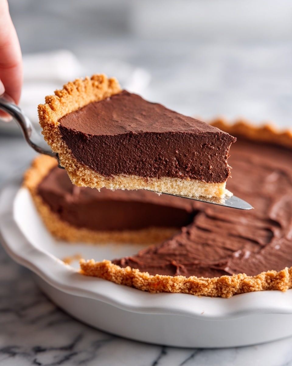 A close-up of a slice being lifted from a chocolate pie with a woman's hand holding a metal pie server. The pie has two main layers: a thick, deep brown, slightly cracked chocolate top layer that looks soft and rich, and a lighter brown crust layer at the bottom with a rough, golden texture and crimped edges. The pie is in a white pie dish, and the background shows a white marbled surface. Photo taken with an iphone --ar 4:5 --v 7