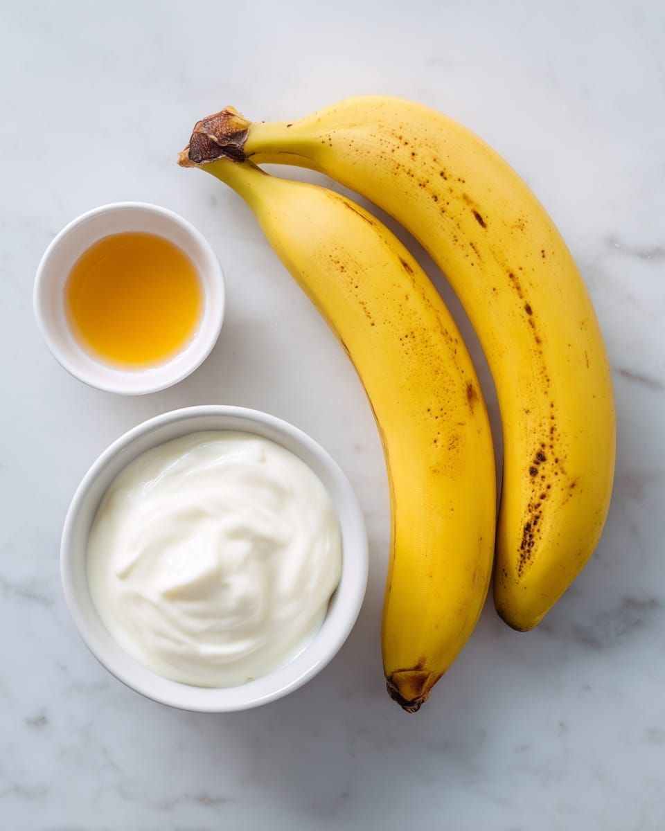 The image shows two ripe yellow bananas with some brown spots, placed on a white marbled surface. Below the bananas, there is a small white bowl filled with creamy white Greek yogurt, reflecting a soft texture. To the left of the yogurt, there is a small white bowl containing a golden brown liquid, labeled vanilla. The items are arranged simply and spaced apart on the marbled background. photo taken with an iphone --ar 4:5 --v 7