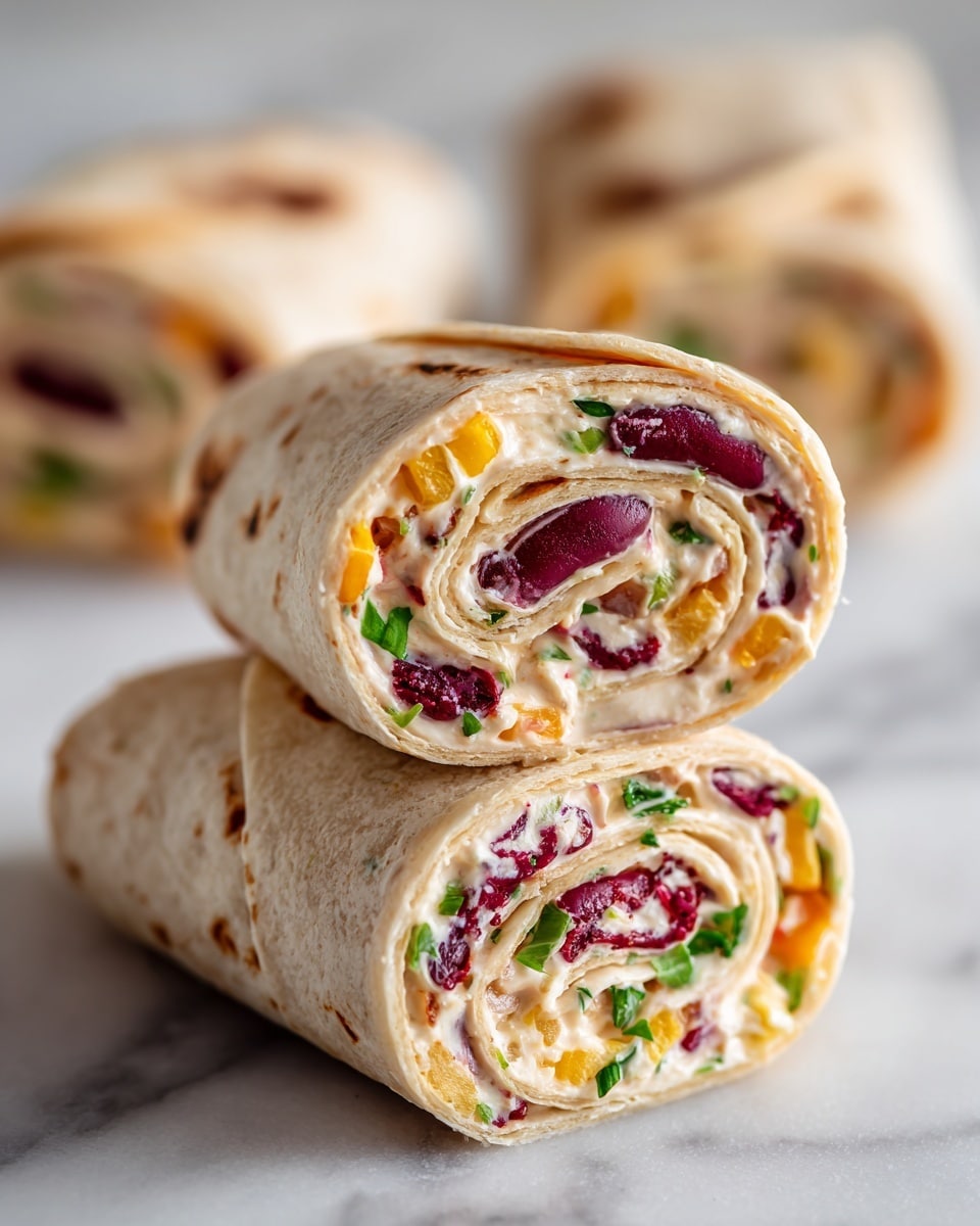 The image shows two pinwheel wraps stacked on top of each other on a white marbled surface. Each wrap has a soft, light beige tortilla outer layer wrapped around multiple fillings. Inside, there is a creamy white spread mixed with slices of dark red beans, small bits of orange-yellow cheese, bright red pepper pieces, and some green herbs. The fillings are tightly rolled, creating colorful swirls in each pinwheel slice. The focus is sharp on the top pinwheel, showing the detailed texture of the creamy spread and beans, while the background is softly blurred with more pinwheels faintly visible. Photo taken with an iphone --ar 4:5 --v 7