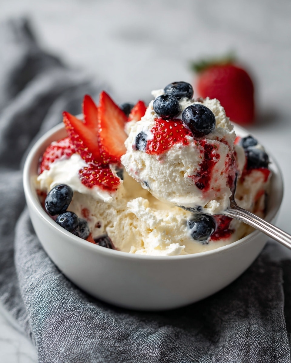A close-up of a white bowl filled with three main layers: the bottom layer is white fluffy cream, the middle layer shows pieces of bright red strawberries and dark blue blueberries mixed into the cream, and the top layer has more fresh strawberry slices and whole blueberries placed on top. A silver spoon holds a scoop showing the three layers clearly, with the colorful berries contrasting against the white cream. The bowl is resting on a gray textured cloth, all placed on a white marbled background. Photo taken with an iphone --ar 4:5 --v 7