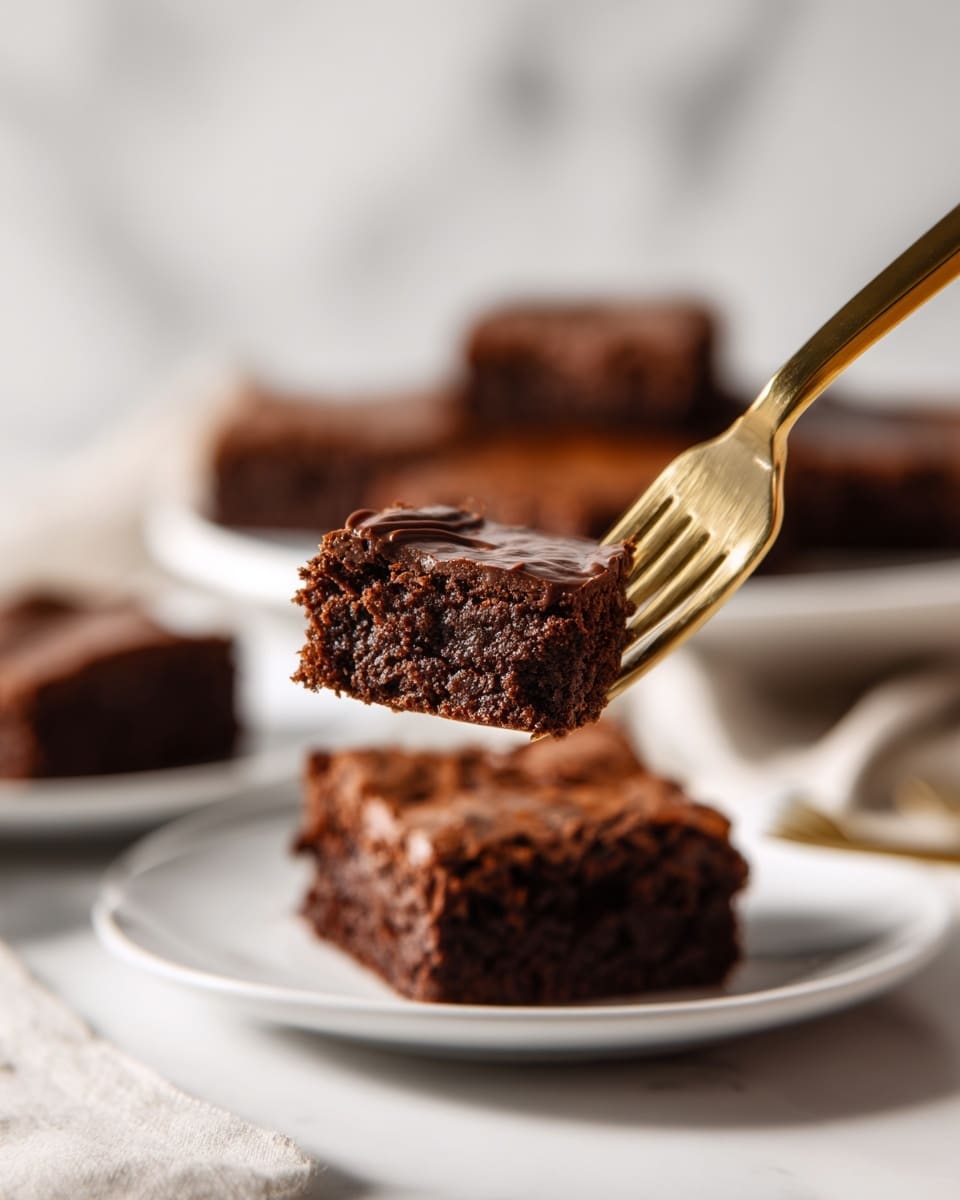 A close-up view of a moist dark brown chocolate brownie piece held on a gold fork. The brownie has a soft texture with tiny air holes inside and a shiny, smooth chocolate layer on top. Behind the fork, there are more square brownie pieces placed on white plates against a white marbled surface, softly blurred. The scene feels warm and inviting, focusing on the rich, dark chocolate color and texture of the brownie. Photo taken with an iphone --ar 4:5 --v 7