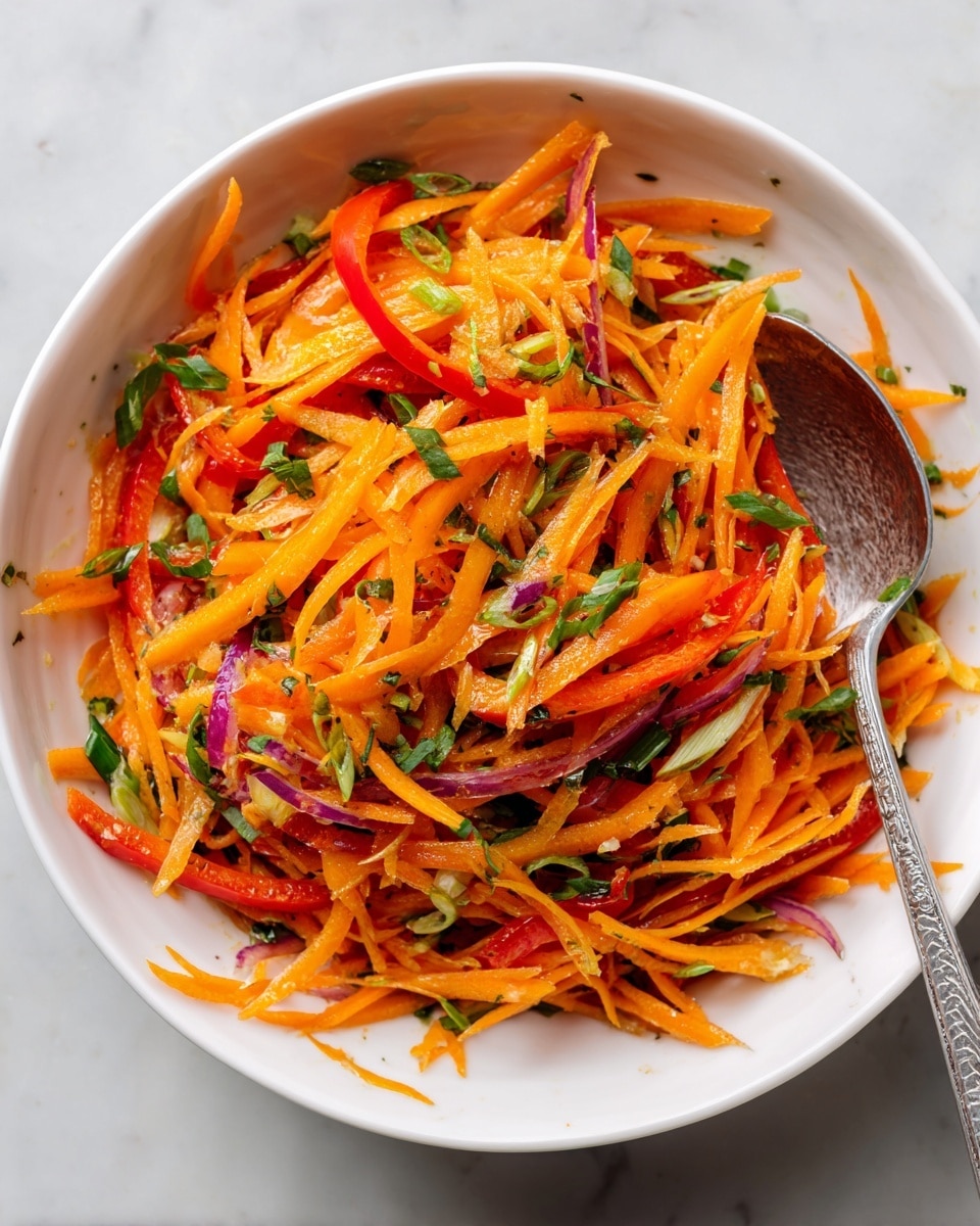 A white bowl filled with a colorful salad made of thin orange carrot sticks mixed with slightly thicker orange and red bell pepper strips, accented by small green onion pieces scattered throughout. The texture shows some finely chopped herbs giving a fresh and varied look. A silver spoon rests in the bowl, leaning on the right side, ready for serving. The scene is set on a white marbled surface, providing a clean and bright contrast to the vivid colors of the salad. Photo taken with an iphone --ar 4:5 --v 7