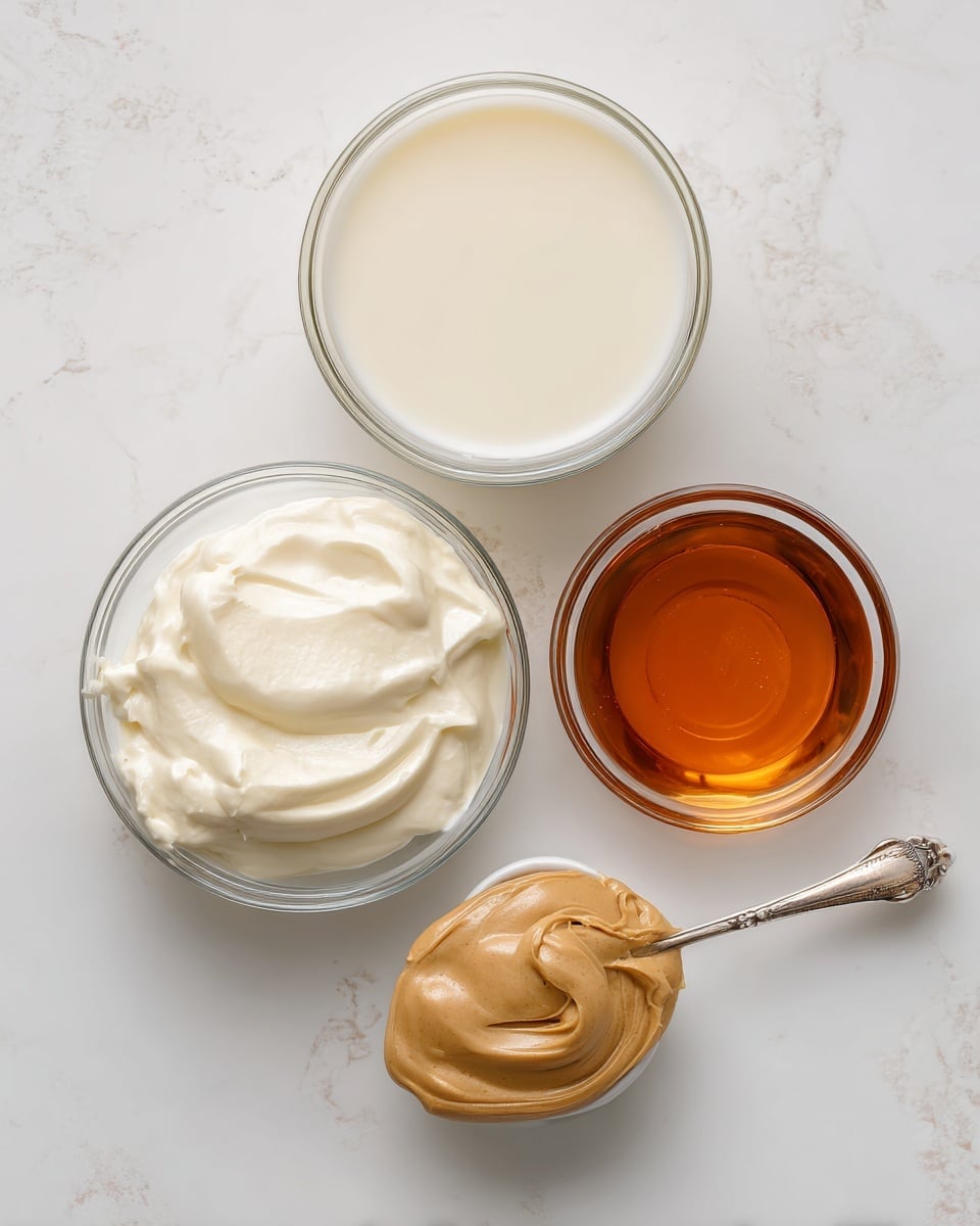 The image shows four clear glass bowls arranged on a white marbled surface, each containing a different ingredient. The top bowl holds a smooth, light off-white liquid labeled milk. Below it to the left is another bowl filled with thick, white heavy cream that has a creamy texture. To the right is a smaller bowl with a transparent amber liquid labeled vanilla extract. Next to it, a spoon holds a dollop of light brown cookie butter with a smooth, spreadable texture. The bowls are arranged close to each other, clearly showing the color and texture of each ingredient, photo taken with an iphone --ar 4:5 --v 7