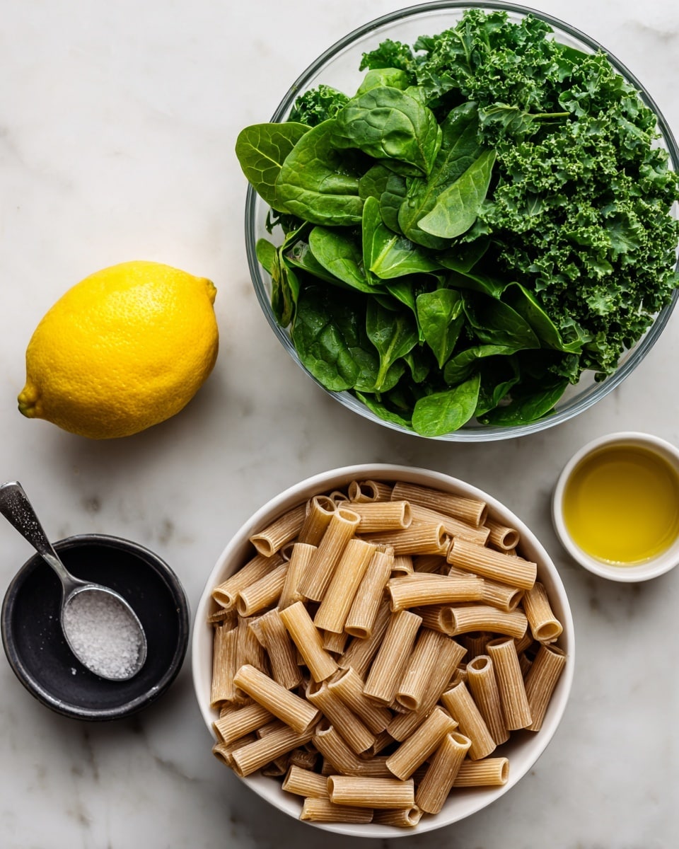 A clear glass bowl filled with two layers of leafy greens: chopped kale on the left side and fresh spinach leaves on the right side, both bright green and textured. Below this, a white bowl is full of uncooked short tube-shaped pasta, light brown in color, arranged loosely. To the left of the bowls is a whole lemon, bright yellow with a textured skin. Above the lemon is a small white bowl containing golden yellow olive oil. Below the lemon is a small black bowl with coarse salt and a metal measuring spoon resting inside. The items are placed on a white marbled surface. photo taken with an iphone --ar 4:5 --v 7
