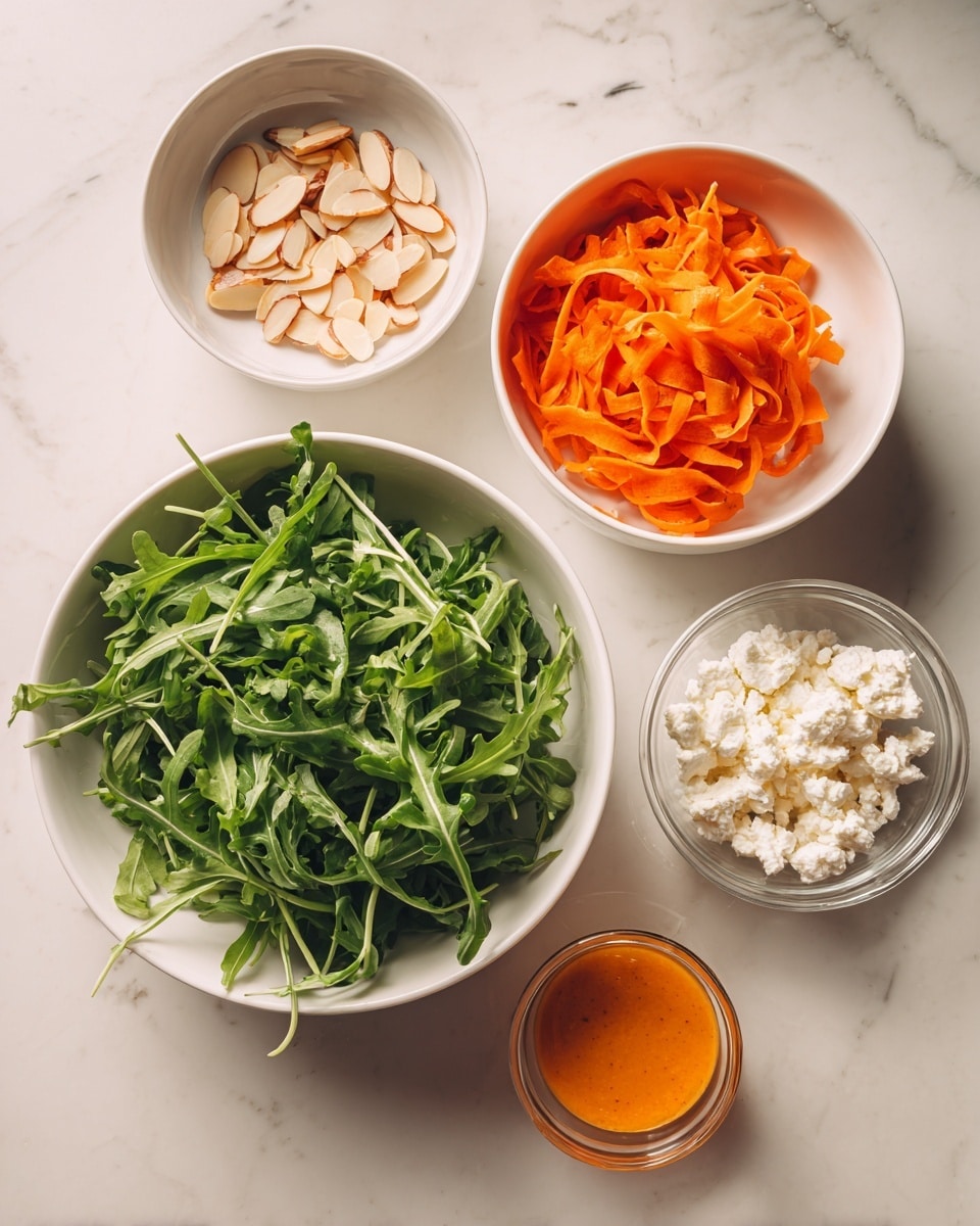 The image shows five white bowls arranged on a white marbled surface. The largest bowl at the bottom center is filled with fresh green arugula leaves, vibrant and textured with a natural leafy shape. To the top right, a medium bowl holds bright orange carrot ribbons, thin and curly, piled high. To the top left is a small bowl containing pale, sliced almonds, thin and flat with softly curved edges. Below that, another small bowl is filled with crumbly white goat cheese, with a soft texture and irregular shapes. On the right side, a small glass container holds orange vinaigrette, smooth in texture with a bright, glossy surface. Photo taken with an iphone --ar 4:5 --v 7