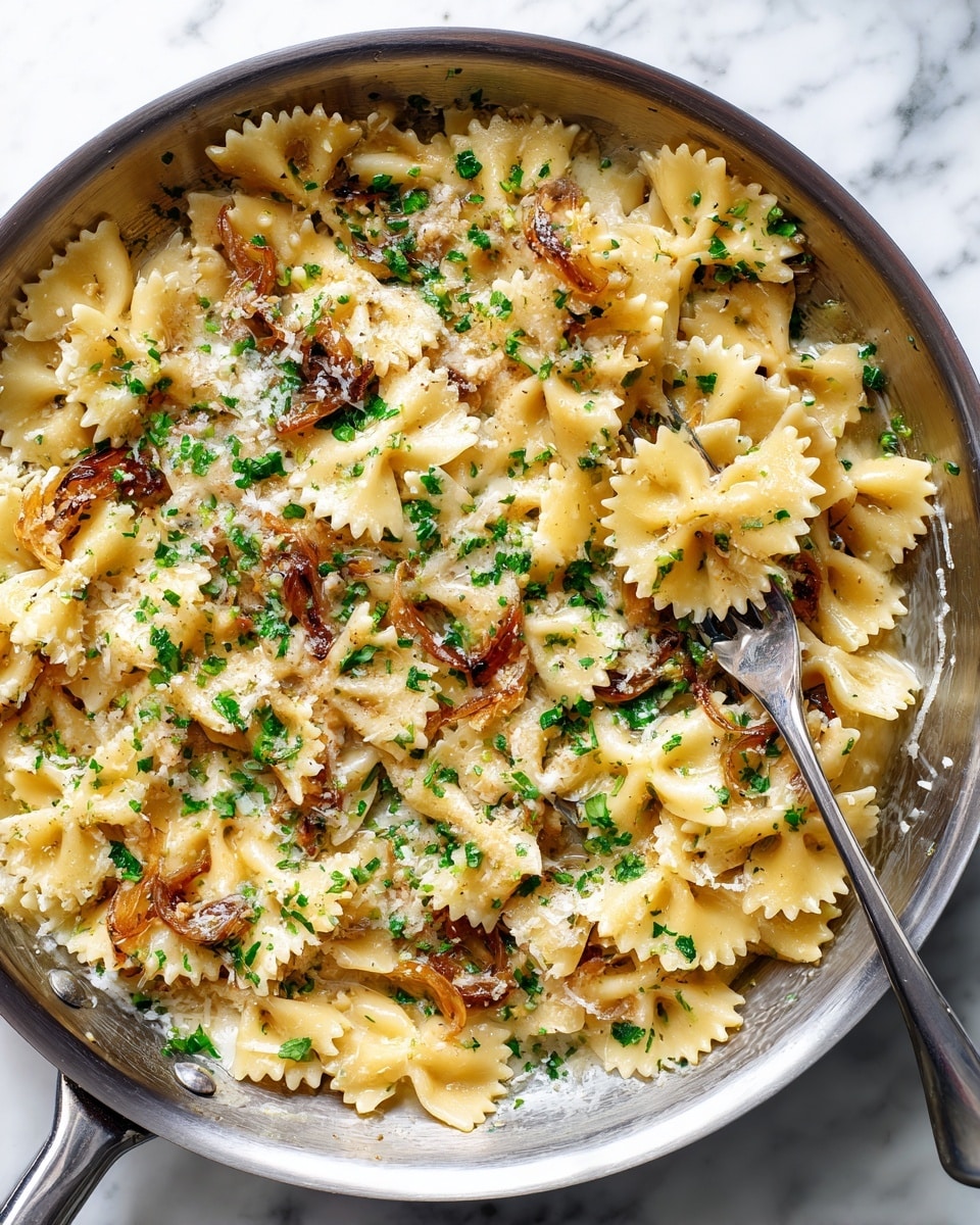 A large silver pan filled with farfalle pasta coated in a light creamy sauce, with a few caramelized onion slices mixed through. The pasta is topped with small sprinkles of green herbs and grated pale yellow cheese scattered unevenly. A silver fork is partially buried on the right side of the dish, lifting some pasta. The pan sits on a white marbled surface. photo taken with an iphone --ar 4:5 --v 7