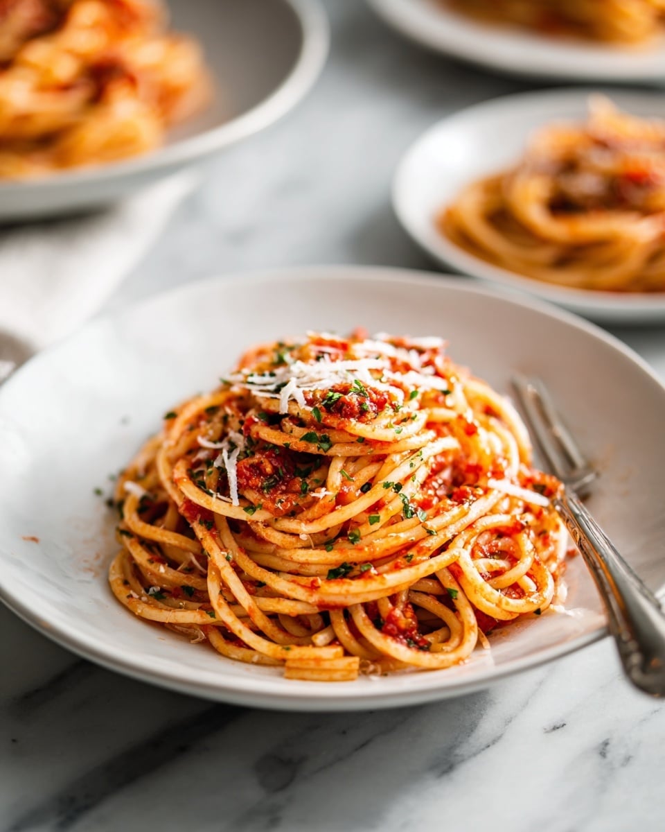 A white plate holds a pile of round spaghetti noodles covered in red tomato sauce, sprinkled with bits of dried herbs and pale shreds of cheese on top. A silver fork stands vertically in the middle of the pasta, with some noodles wound around its tines. Behind this plate, there are blurred white plates with more spaghetti on a surface that has a white marbled texture. photo taken with an iphone --ar 4:5 --v 7