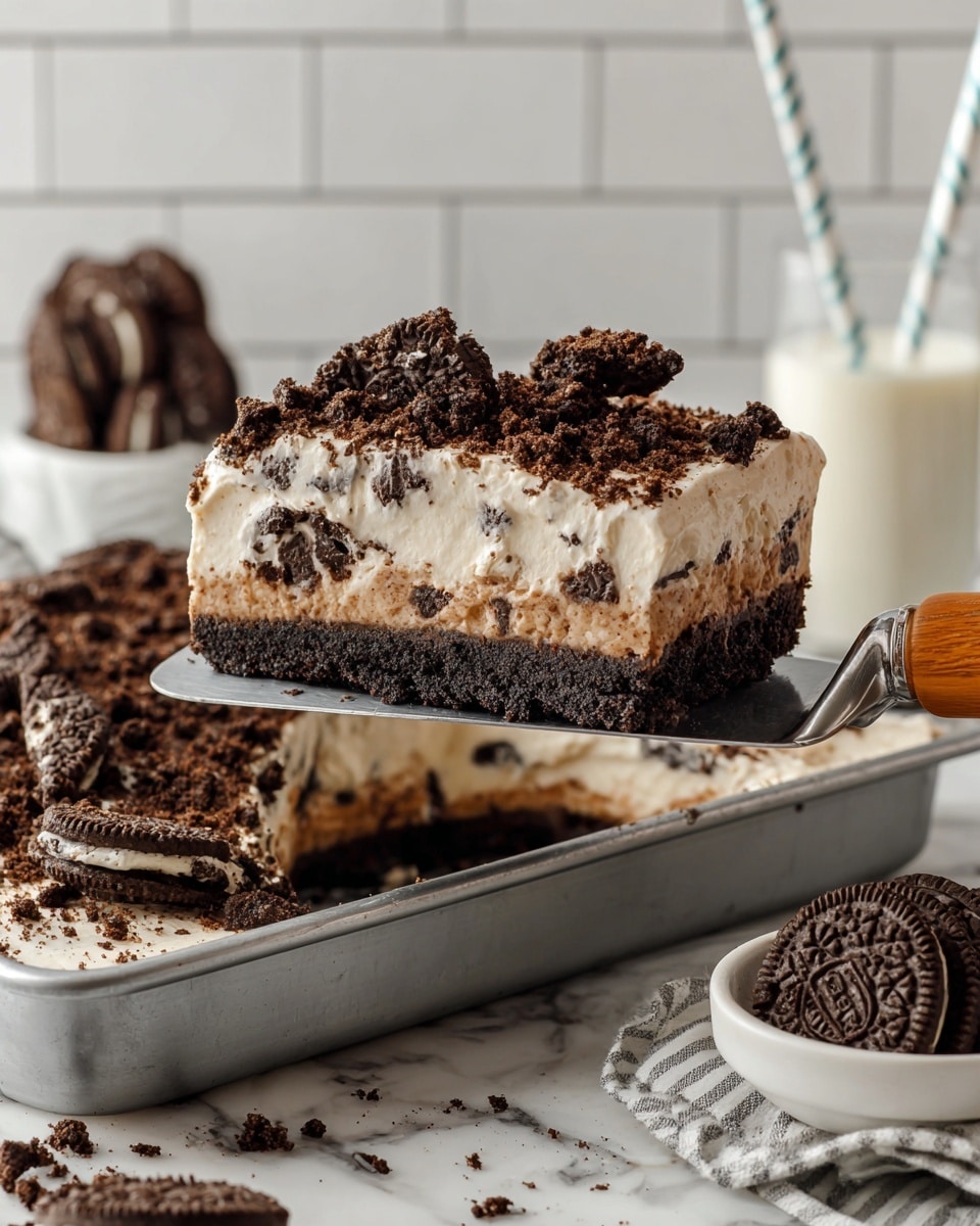 The image shows a thick slice of cookies and cream dessert on a metal spatula with a wooden handle. The dessert has three main layers: a dark brown crumbly cookie crust at the bottom, a light creamy middle layer mixed with small cookie pieces, and a top layer made of crushed dark brown cookies scattered unevenly. The dessert is held above a large pan filled with more of the same crushed cookies topping. In the background, there is a white marbled surface, a glass of milk with a striped straw, and a small white bowl with more whole dark cookies. The overall setting is bright and clean with a white tiled wall. Photo taken with an iphone --ar 4:5 --v 7