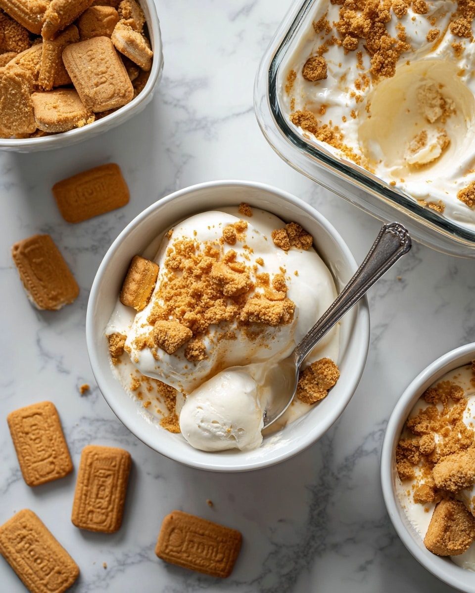 The image shows a creamy dessert in a small white bowl, with one visible layer of smooth white cream, topped with crumbled golden-brown cookie pieces scattered unevenly on the surface. A silver spoon is placed inside the bowl, partially submerged in the cream. Next to it, there is another white bowl filled with the same creamy dessert and cookie crumbles on top. There is also a clear glass baking dish with several spoonfuls of the dessert. Around the bowls, there are whole and packaged golden-brown Lotus Biscoff cookies on a white marbled surface. The photo taken with an iphone --ar 4:5 --v 7