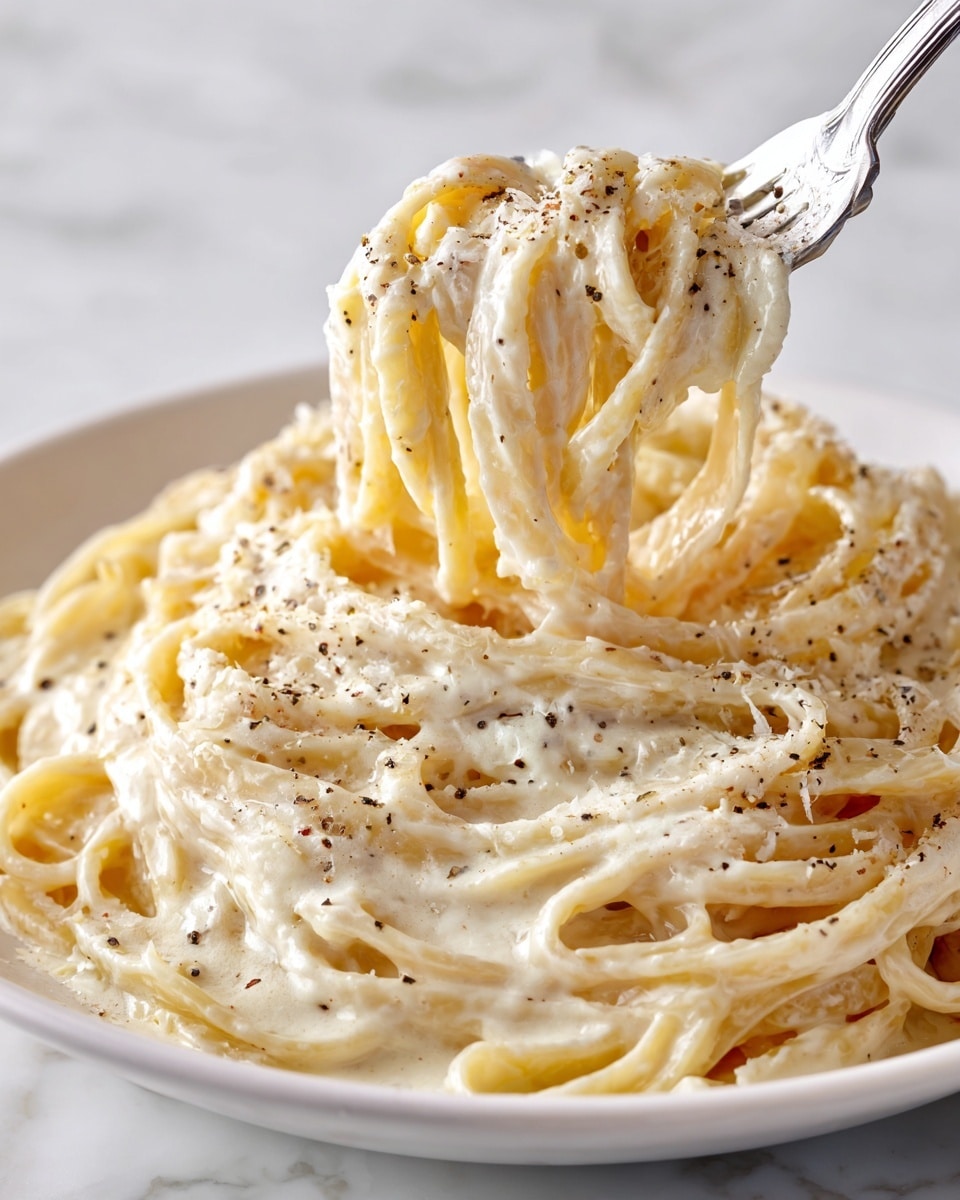 A close-up view of a white round pot filled with creamy fettuccine pasta, the noodles are long, flat, and coated in a smooth, white sauce. Small bits of green herbs are scattered on top, adding light green color contrast. Some pasta strands are twirled around silver tongs resting inside the pot. The pot handle is visible, and the scene is set on a white marbled surface with some fresh green herbs nearby. photo taken with an iphone --ar 4:5 --v 7