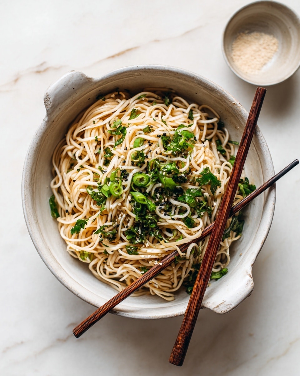 A white bowl filled with light brown noodles covered with small pieces of green herbs and bits of light beige chicken. Two dark brown chopsticks are held over the noodles by a woman's hand. The bowl sits on a white marbled surface with a small round condiment dish visible near the bottom edge of the image. photo taken with an iphone --ar 4:5 --v 7