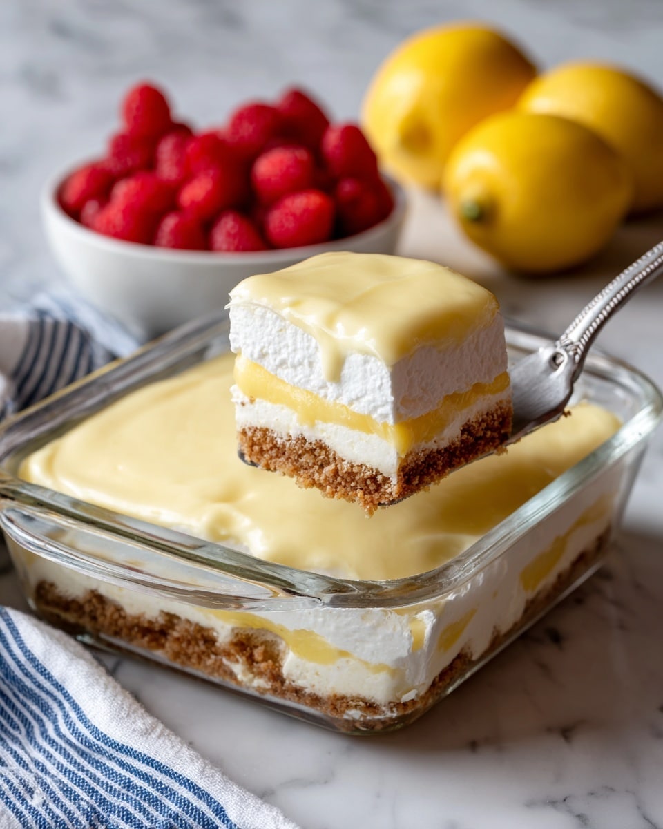 A glass rectangular dish shows a layered dessert with four clear layers: the bottom is a brown crumb base, followed by a thick pale yellow creamy layer, then a white fluffy cream layer, and topped with a smooth, pale yellow layer that looks like lemon cream. A piece of dessert is lifted by a metal spatula, showing the clean layer separation and soft textures. Next to the dish, a small white bowl filled with fresh red raspberries and two whole yellow lemons rest on a white marbled surface, with a hint of a blue and white striped cloth nearby. photo taken with an iphone --ar 4:5 --v 7
