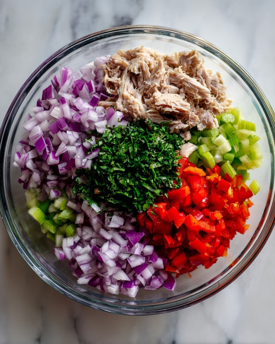The image shows a clear glass bowl with five distinct layers of ingredients arranged in separate sections. At the front left, finely chopped red onions with a light purple and white color are spread. To their right, there is a shredded light beige meat layer. Behind the onions is a layer of chopped bright red bell pepper pieces. Next to the red pepper, there is a layer of chopped pale green celery. In the center, on top of some of the other layers, sits a small pile of finely chopped dark green fresh herbs. The bowl is placed on a white marbled surface. photo taken with an iphone --ar 4:5 --v 7