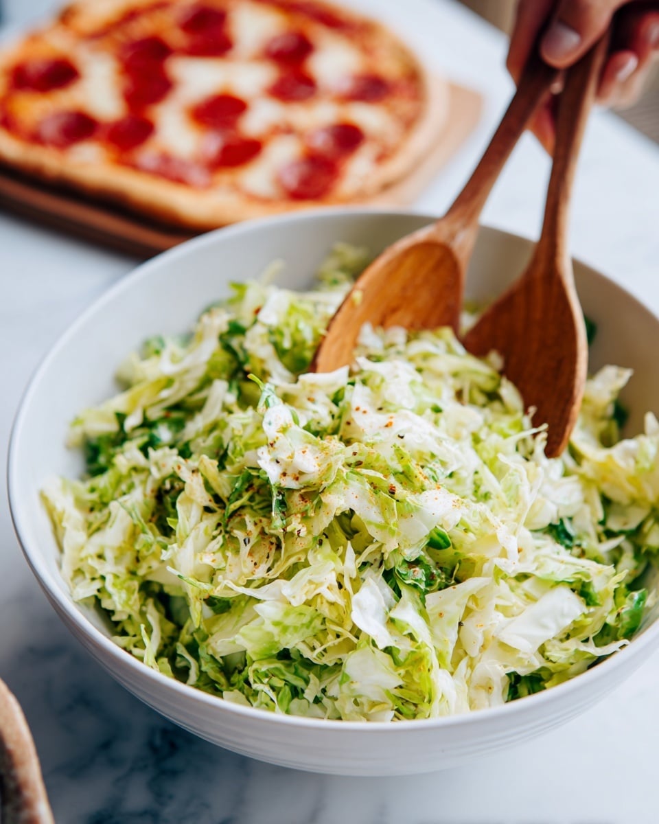 A close-up view showing a white bowl filled with chopped cabbage salad, which has a light green and white color with bits of seasoning sprinkled on top. Two wooden salad spoons are scooping the cabbage from the bowl, with a woman's hand holding one of the spoons from above. In the background, there is a blurred rectangular pizza with tomato sauce, melted cheese, and round pepperoni pieces. The whole scene is set on a white marbled surface. photo taken with an iphone --ar 4:5 --v 7