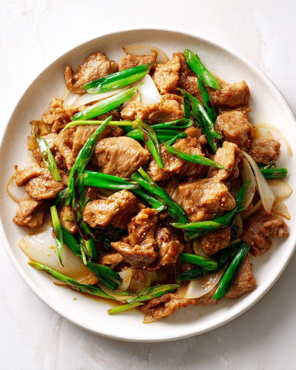 The dish is served on a white round plate, showing several layers of stir-fried pieces of cooked meat that are light brown and slightly shiny from sauce, mixed with thick, translucent white onion slices and bright green pieces of green onion. The meat pieces have a tender texture with some slight browning on the edges. The vegetables are scattered evenly, adding a fresh contrast with their color and crisp look. The white marbled surface under the plate gives a clean and fresh background. Photo taken with an iphone --ar 4:5 --v 7