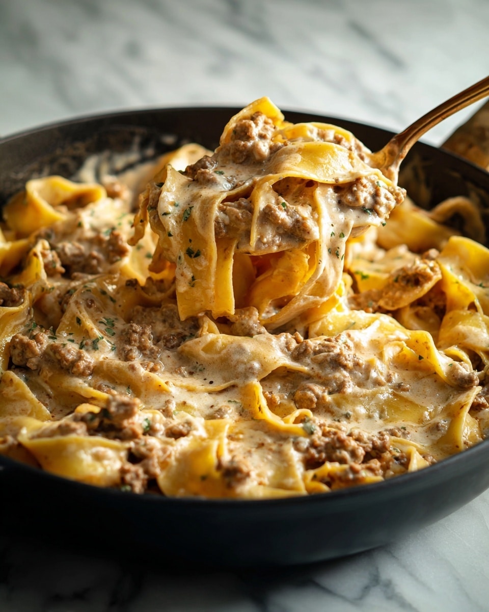 The image shows a dish in a black skillet filled with wide, flat pasta layered with a thick, creamy light brown sauce mixed with small bits of ground meat. The sauce has a smooth texture and clings to the pasta, stretching slightly as a spoon lifts a portion from the skillet. The pasta is soft and partly wavy at the edges. The scene is set against a white marbled surface with soft lighting, highlighting the rich, creamy texture and warm colors of the dish. photo taken with an iphone --ar 4:5 --v 7