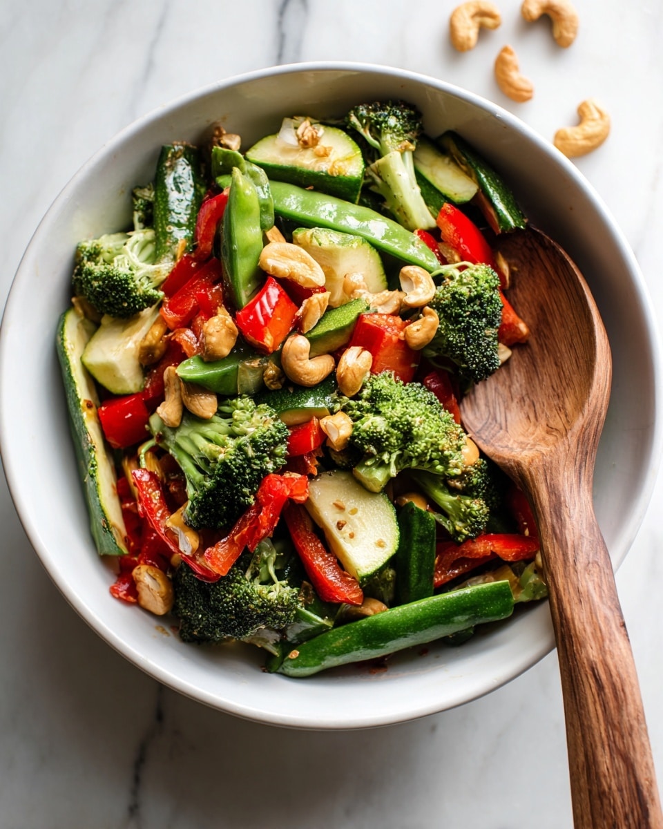 A white bowl filled with a colorful mix of fresh vegetables and small pieces of raw chicken. The base layer shows bright green broccoli florets and snap peas with their smooth shiny texture. There are thick dark green zucchini sticks and chunks of vibrant red bell peppers scattered on top. Light brown roasted cashew nuts add a crunchy look to the mix. A long wooden spoon rests inside the bowl, partially covered by the vegetables and chicken. The background is a white marbled surface with a few stray cashew nuts on it. Photo taken with an iphone --ar 4:5 --v 7