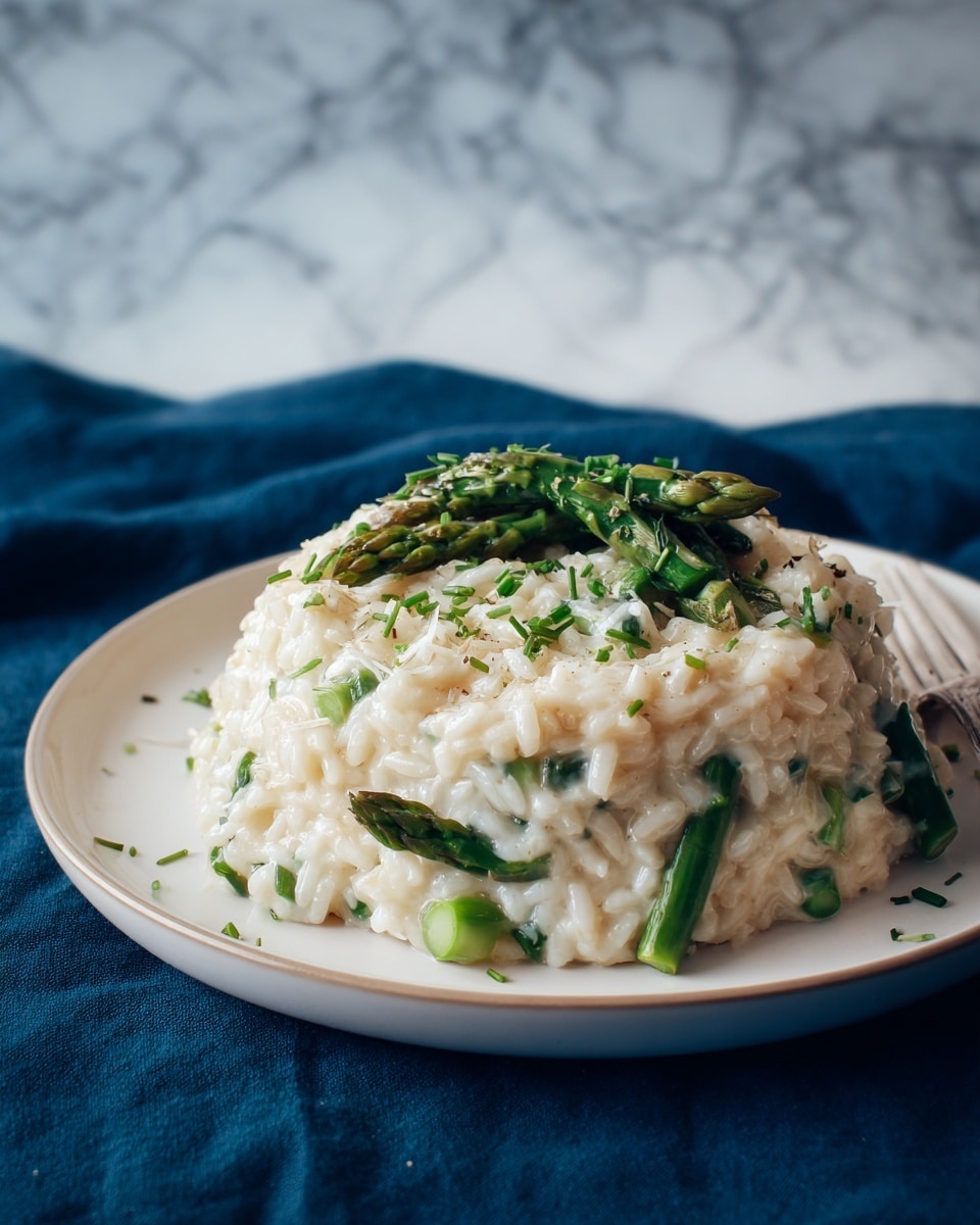 In the image, there is a white deep round plate with a mound of creamy risotto in the center. The risotto is thick and white with a slightly glossy texture. Mixed into the risotto are cut green asparagus pieces that add a fresh green color to the dish. On top of the risotto, there is a sprinkling of finely chopped green herbs, likely chives, adding a bright green contrast. The plate is set on a dark blue cloth surface, but the background is changed to a white marbled texture. The lighting highlights the creaminess of the risotto and the freshness of the green asparagus and herbs. photo taken with an iphone --ar 4:5 --v 7