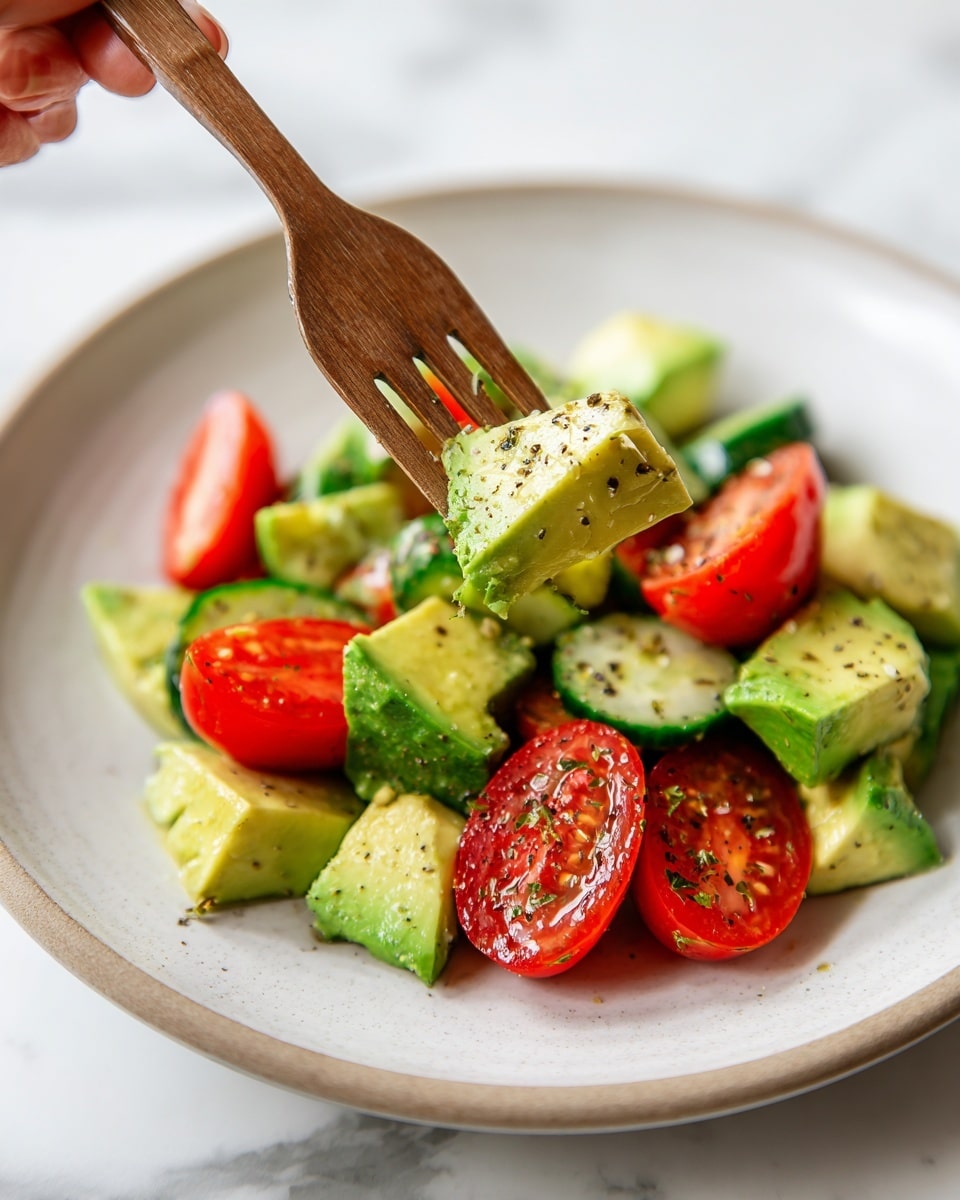 A close-up of a salad shows three main layers on a white plate over a white marbled surface: bright green chunks of avocado with a soft texture and small black seasoning dots, juicy red cherry tomato halves with a shiny appearance on the edges, and vibrant green cucumber slices with darker green edges and seeds in the middle, all mixed together with visible herbs and black pepper on them; a wooden fork held by a woman's hand lifts a piece of each ingredient. Photo taken with an iphone --ar 4:5 --v 7