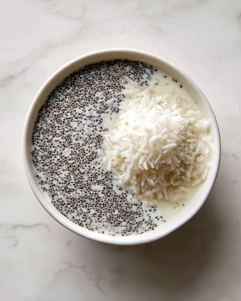 Inside a white bowl, there are two layers: the bottom layer is a creamy white liquid mixed with many small, black chia seeds spread evenly, creating a textured look; on top, there is a small mound of white cooked rice with separate grains that look soft and fluffy, placed near the center. The bowl is set on a white marbled surface. photo taken with an iphone --ar 4:5 --v 7