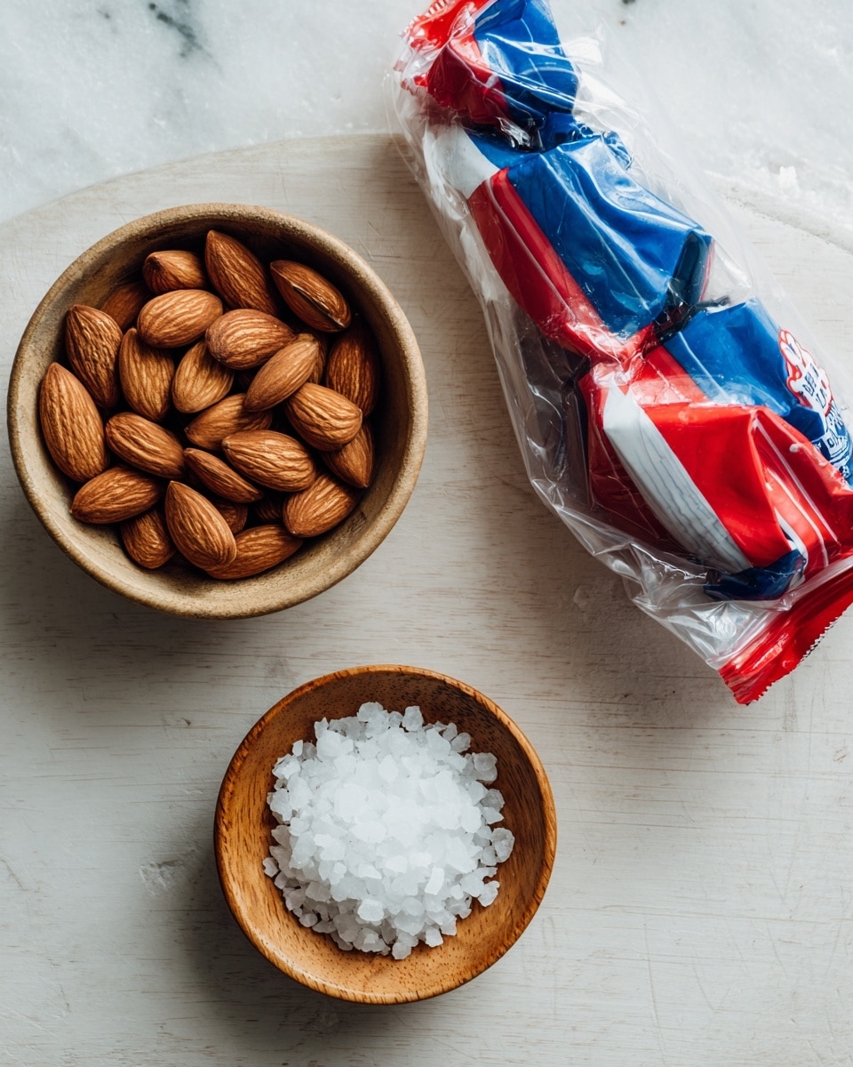 The image shows a top view of three items on a light wooden table with a white marbled texture background. On the left, there is a bowl filled with whole almonds that are brown and smooth in texture. On the right side, there is a bag of semi-sweet baking chocolate chips with red, white, and blue colors on the packaging, partially crumpled. Below, there is a small wooden bowl filled with coarse white sea salt. The arrangement is simple and clean, with natural colors and textures standing out against the background. Photo taken with an iphone --ar 4:5 --v 7